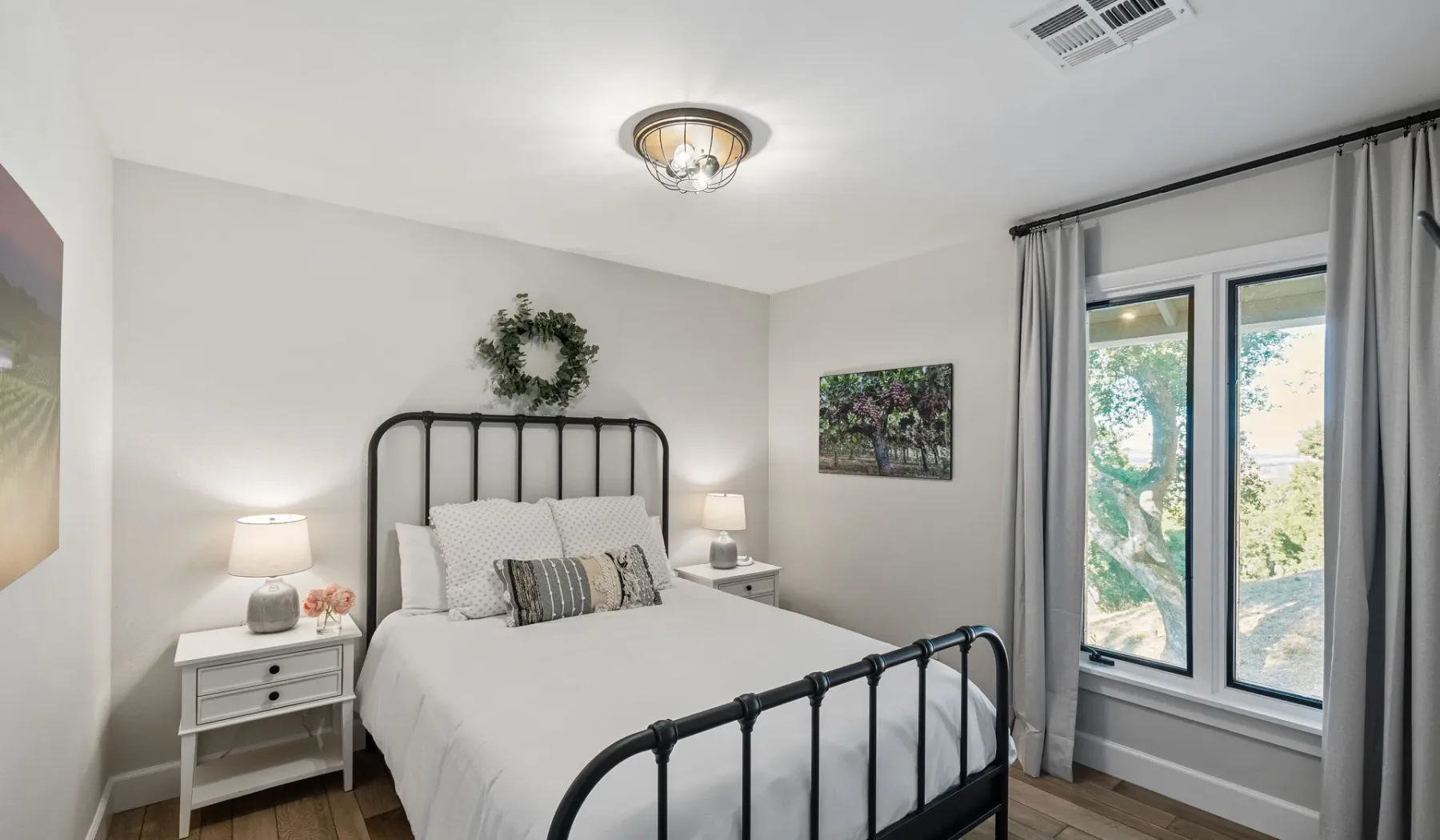 Un dormitorio luminoso con una cama de metal, mesillas y una ventana amplia.