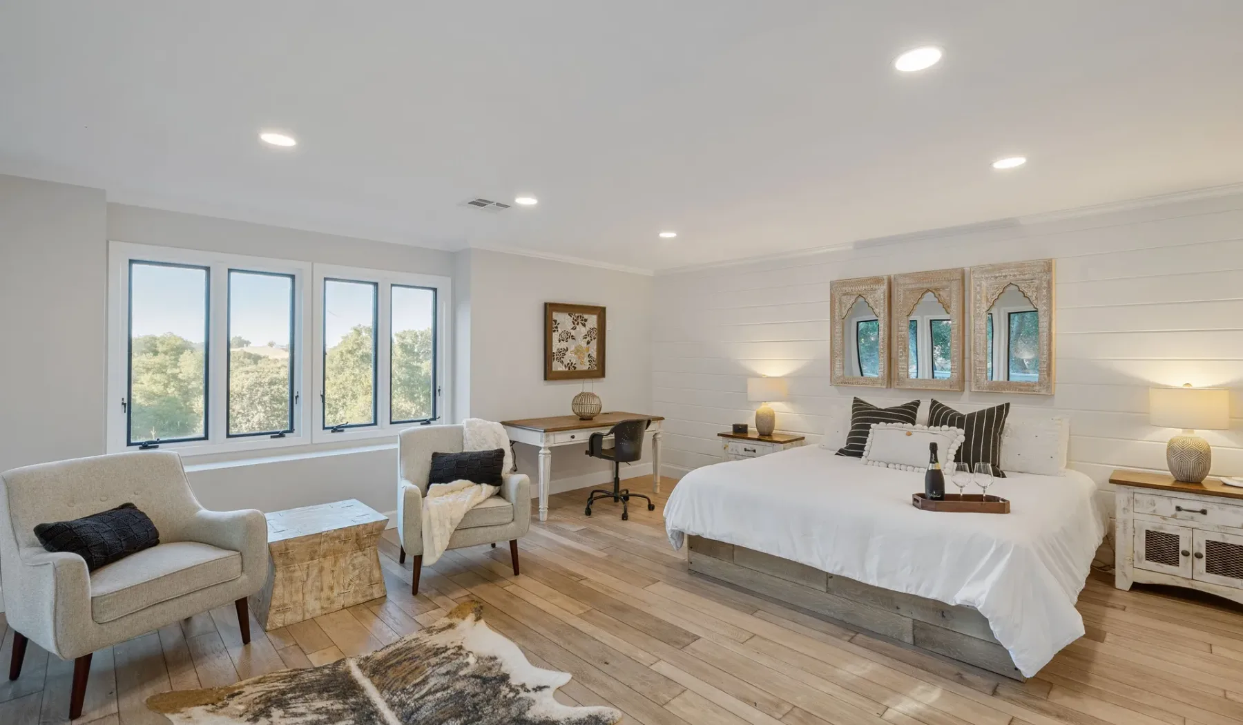 Un dormitorio luminoso con una cama grande, una zona de estar y ventanas amplias.