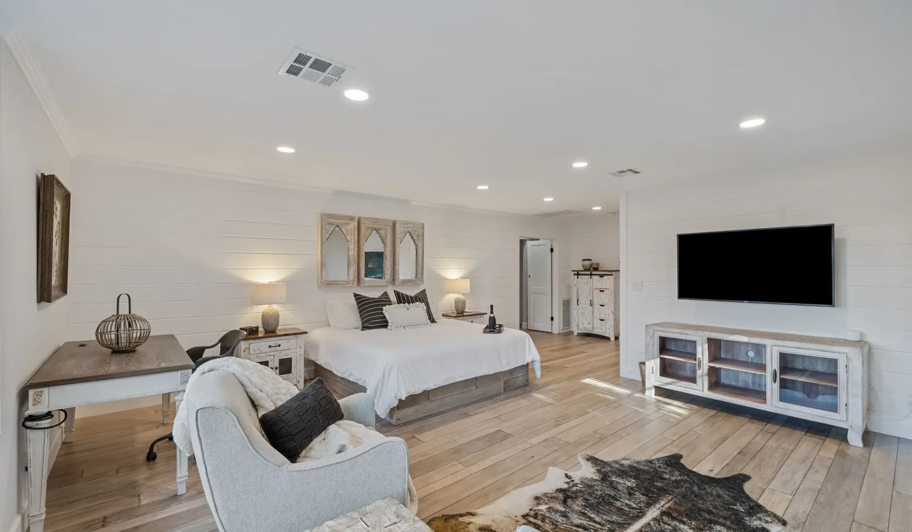 Un dormitorio luminoso con cama, zona de estar y televisor en la pared.