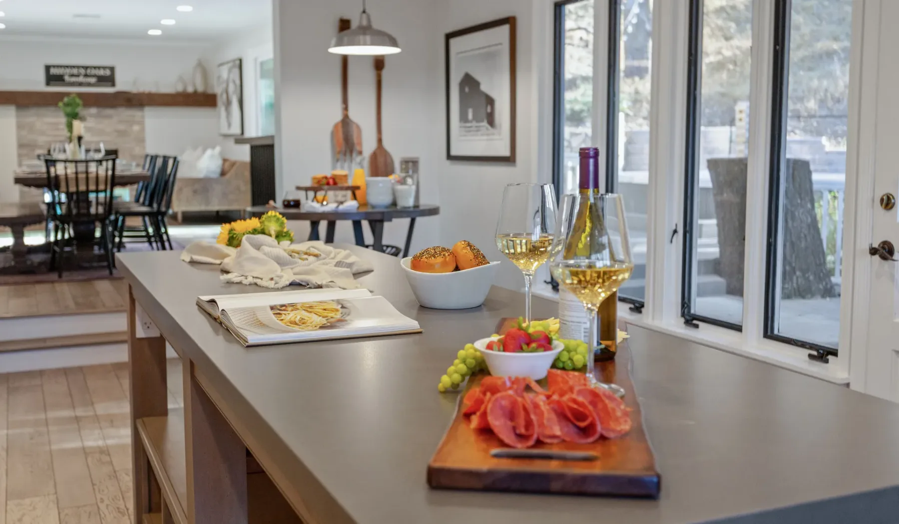 Una isla de cocina con aperitivos y bebidas está junto a grandes ventanas.