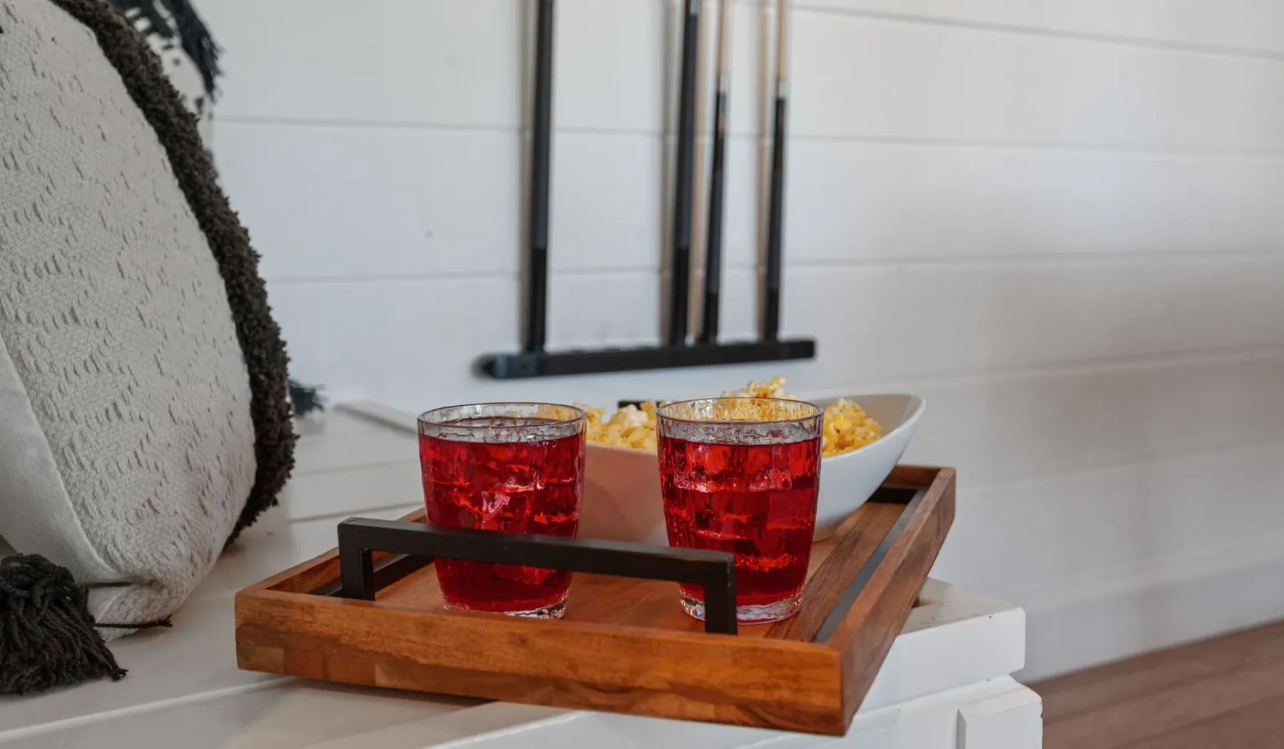Una bandeja de madera contiene bebidas rojas y aperitivos junto a un sofá.