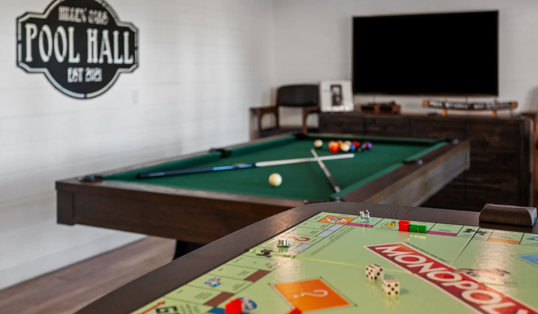 Una sala de juegos con una mesa de billar y un tablero de Monopoly en primer plano.