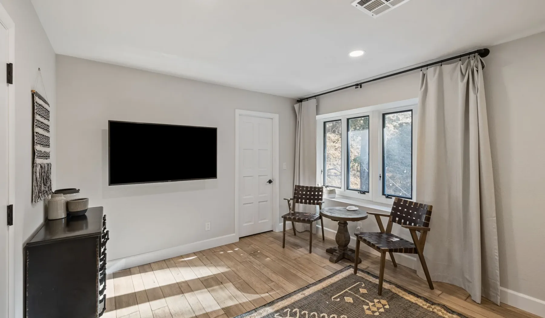 Una sala luminosa con un televisor en la pared y asientos junto a las ventanas.