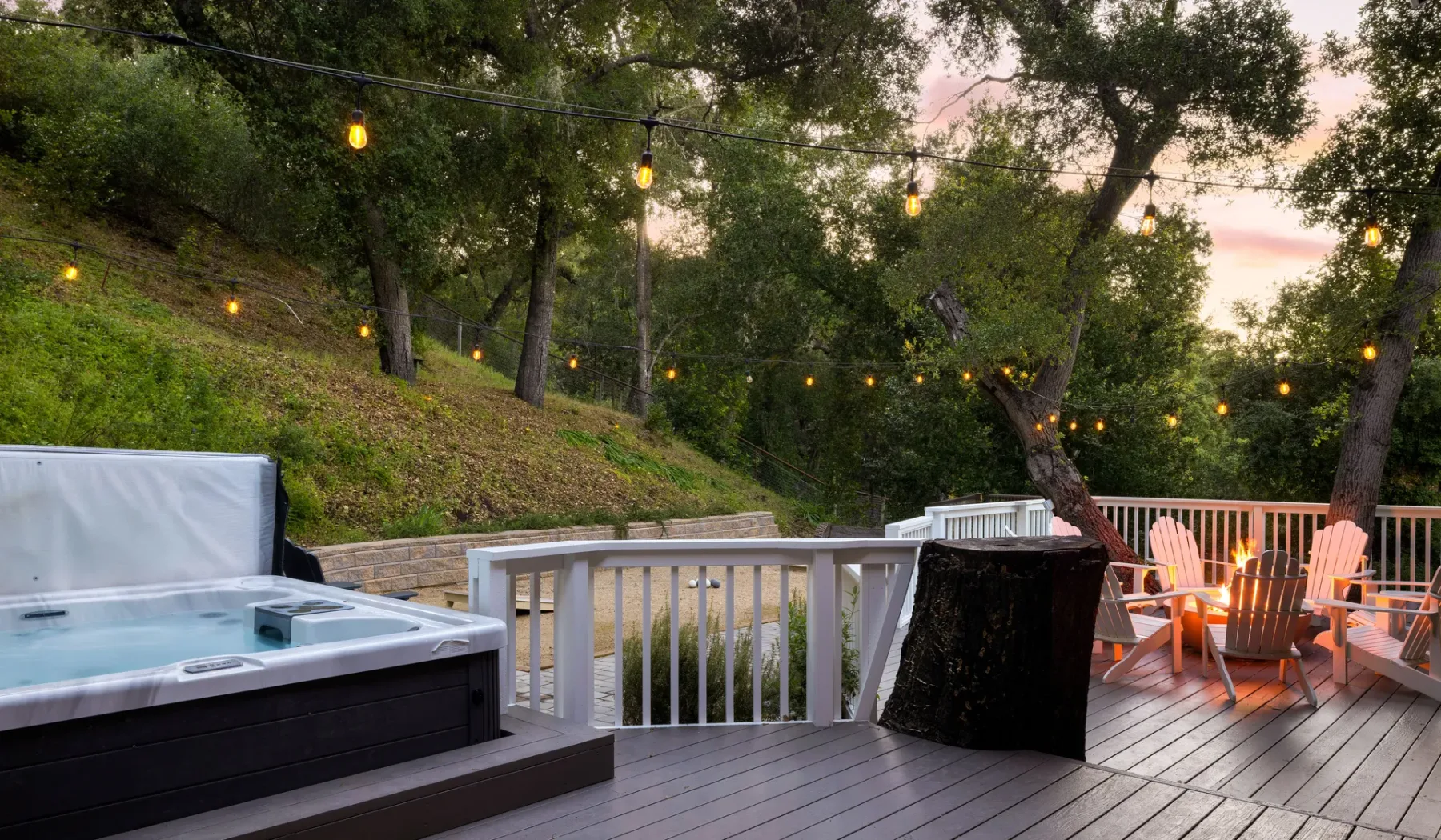 Una terraza exterior con una bañera de hidromasaje y luces entre los árboles.