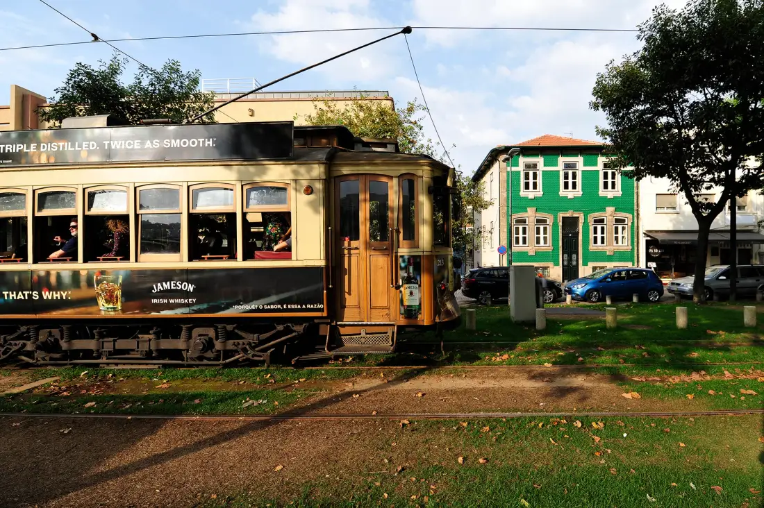 A vintage tram stands beside a green building on a tree-lined street.