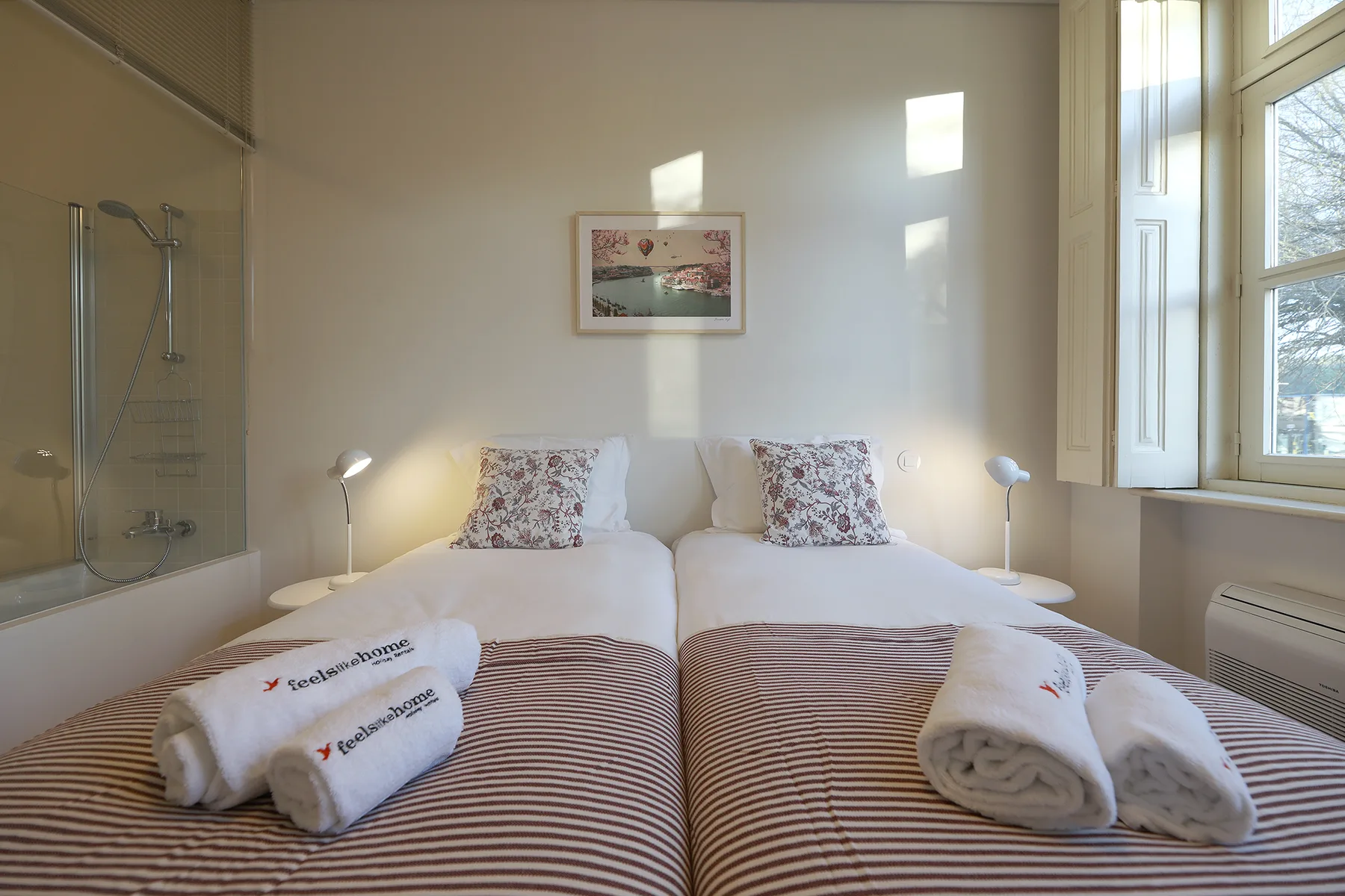 A bedroom with two beds, patterned bedding, and a large window.