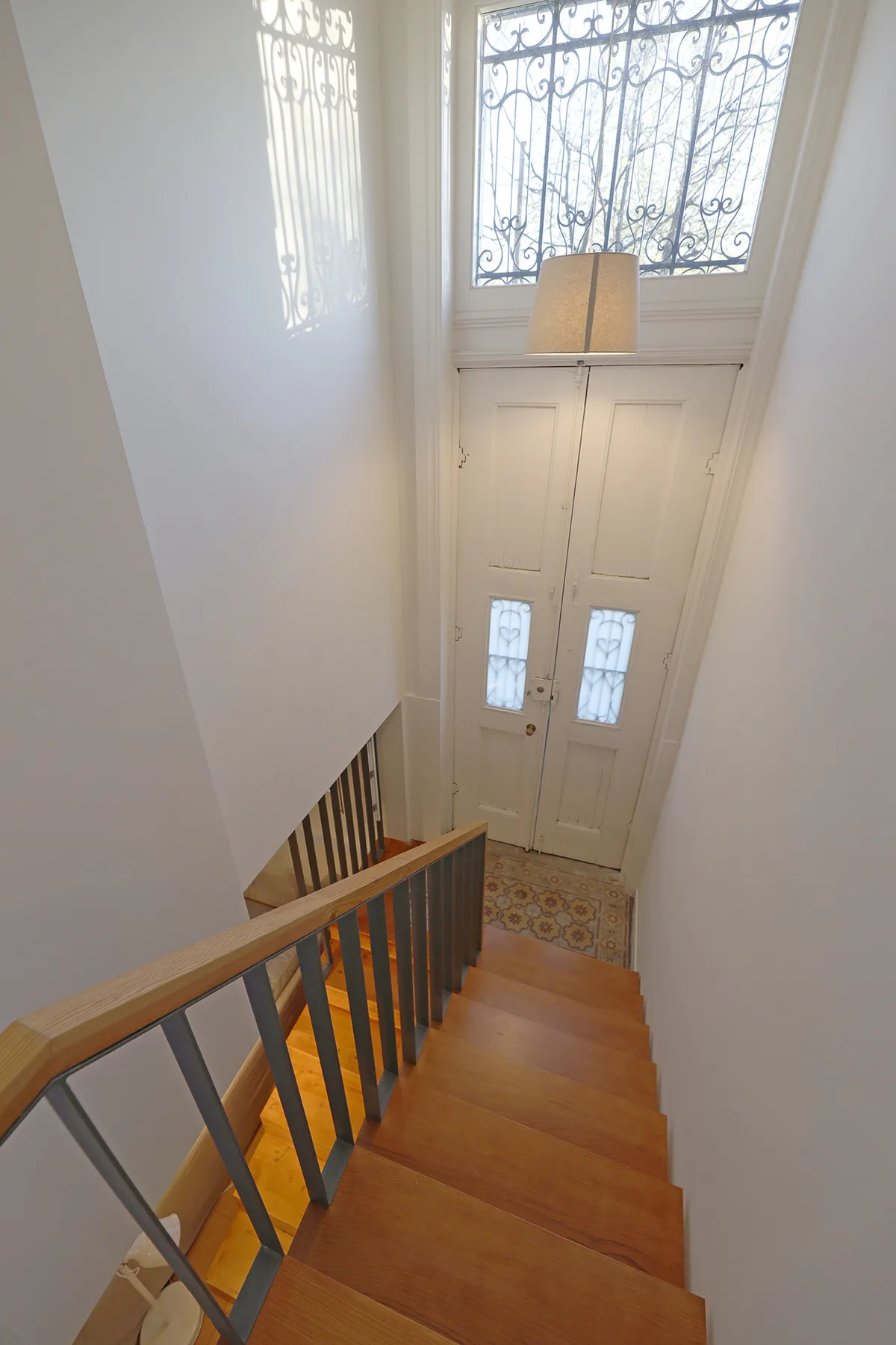 A staircase descends toward a white entry door beneath a decorative window.