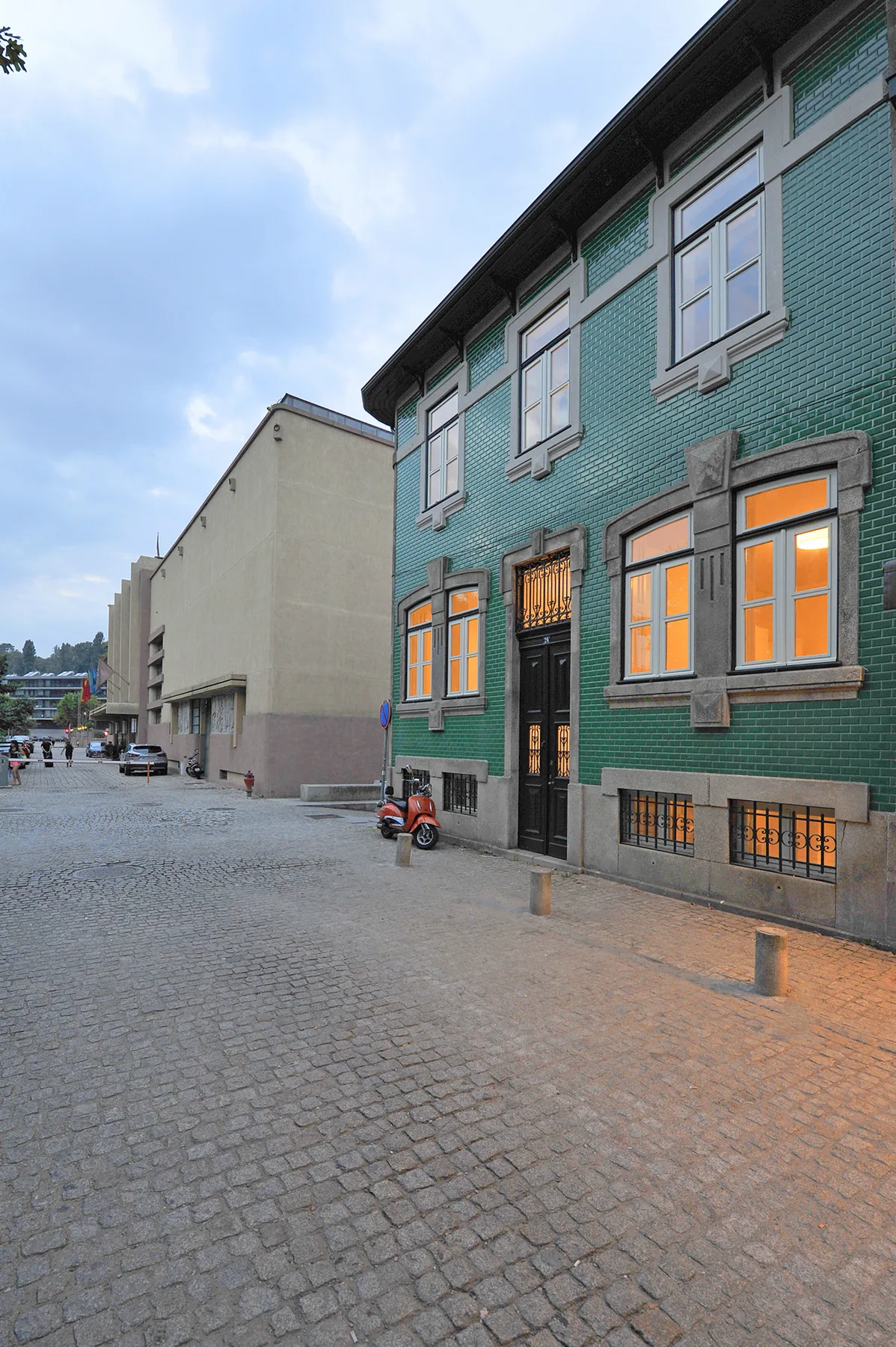 A green tiled building faces a cobblestone street at dusk.