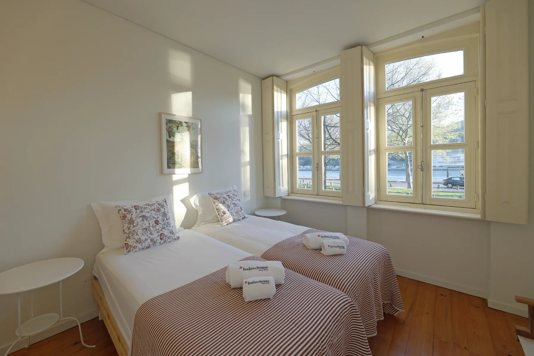 A bright bedroom with two beds beside large windows.