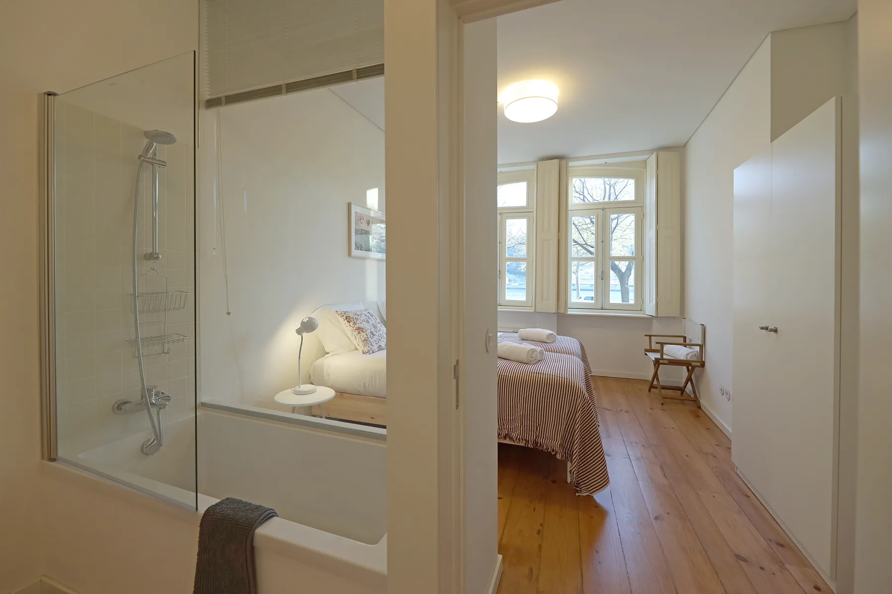 A bedroom with a bed and windows, viewed beside a bathroom shower.