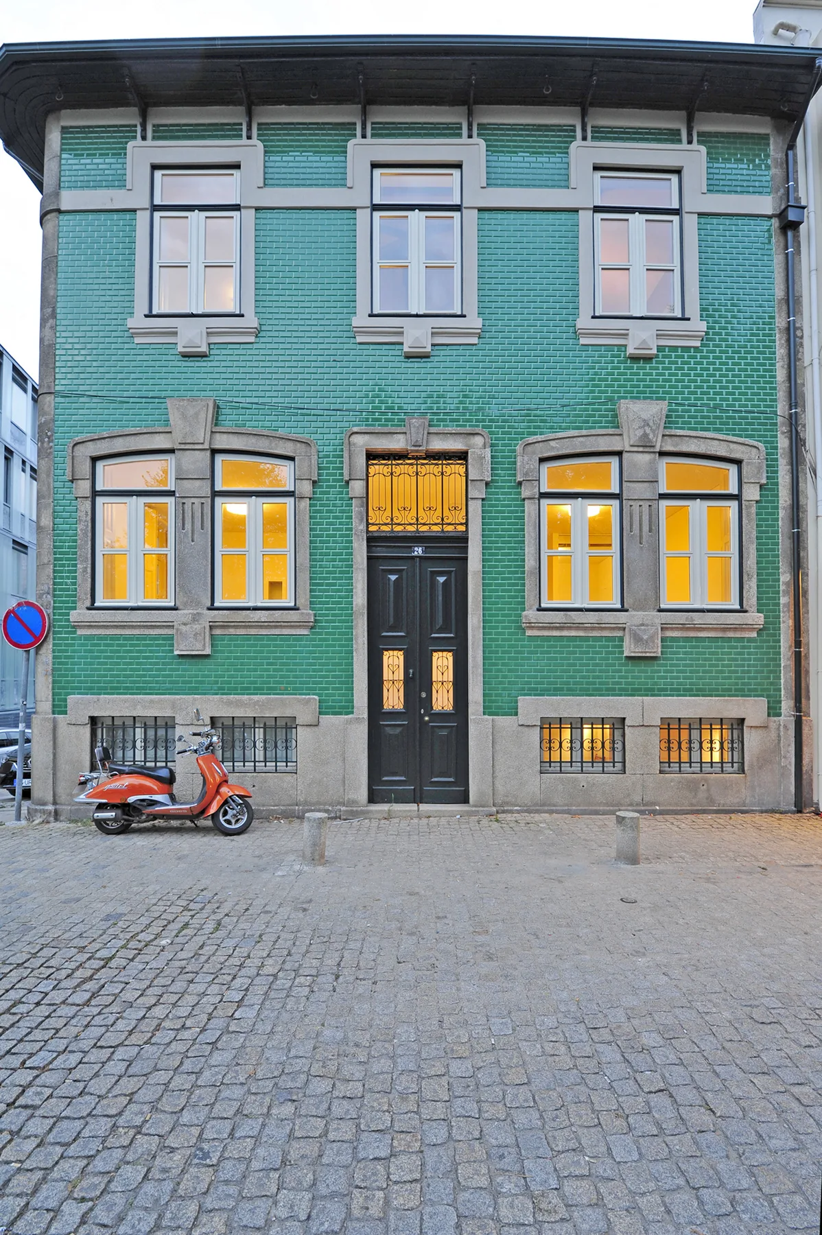 A green-tiled building facade with a central entrance and lit windows.