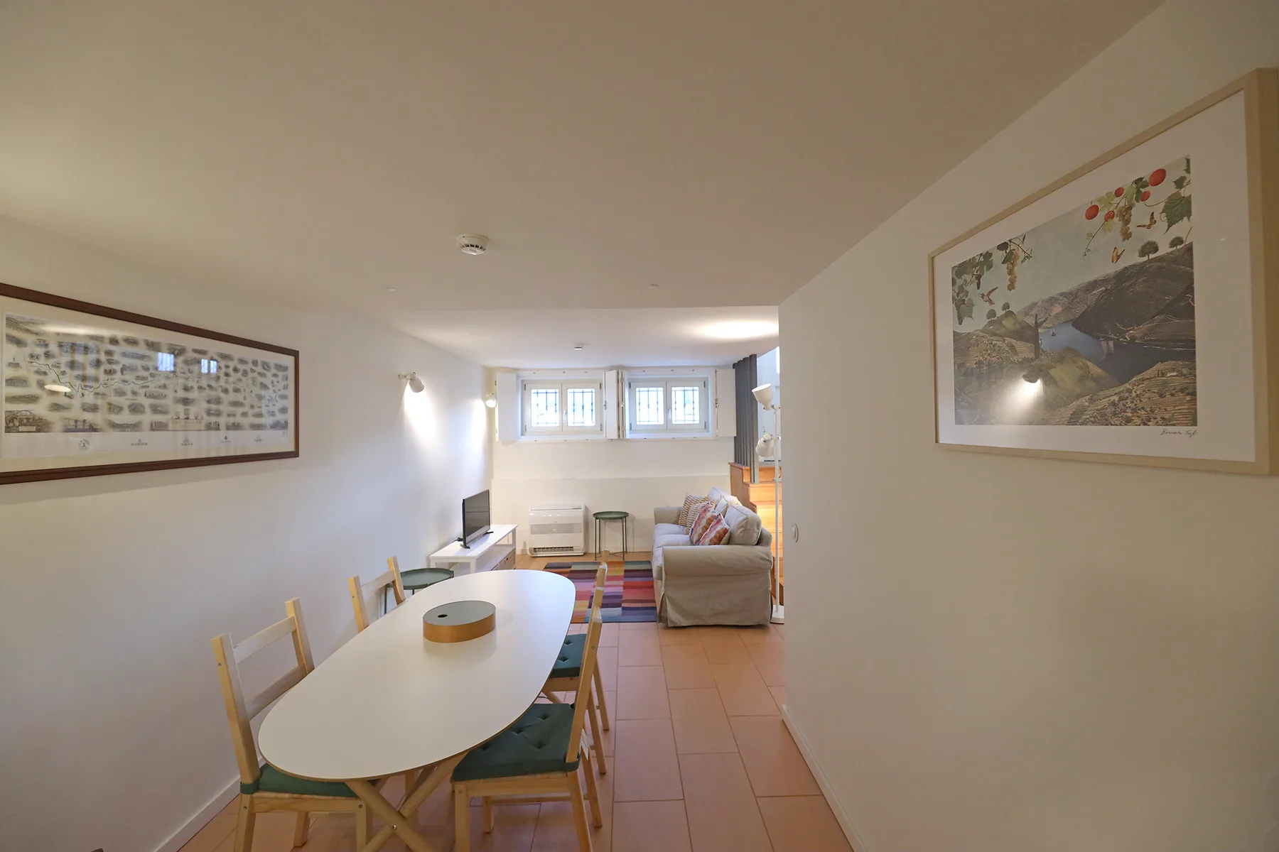 A dining area opens into a living room with a sofa and small windows.