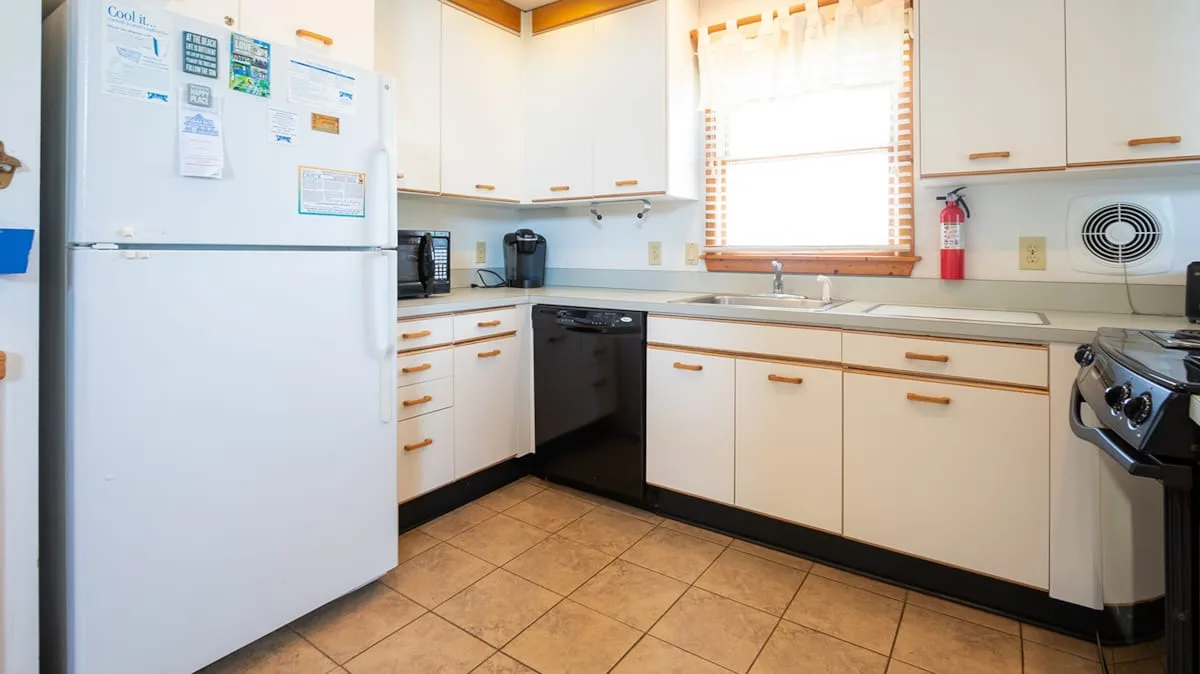 Una cocina luminosa con gabinetes blancos, un refrigerador y una ventana sobre el fregadero.