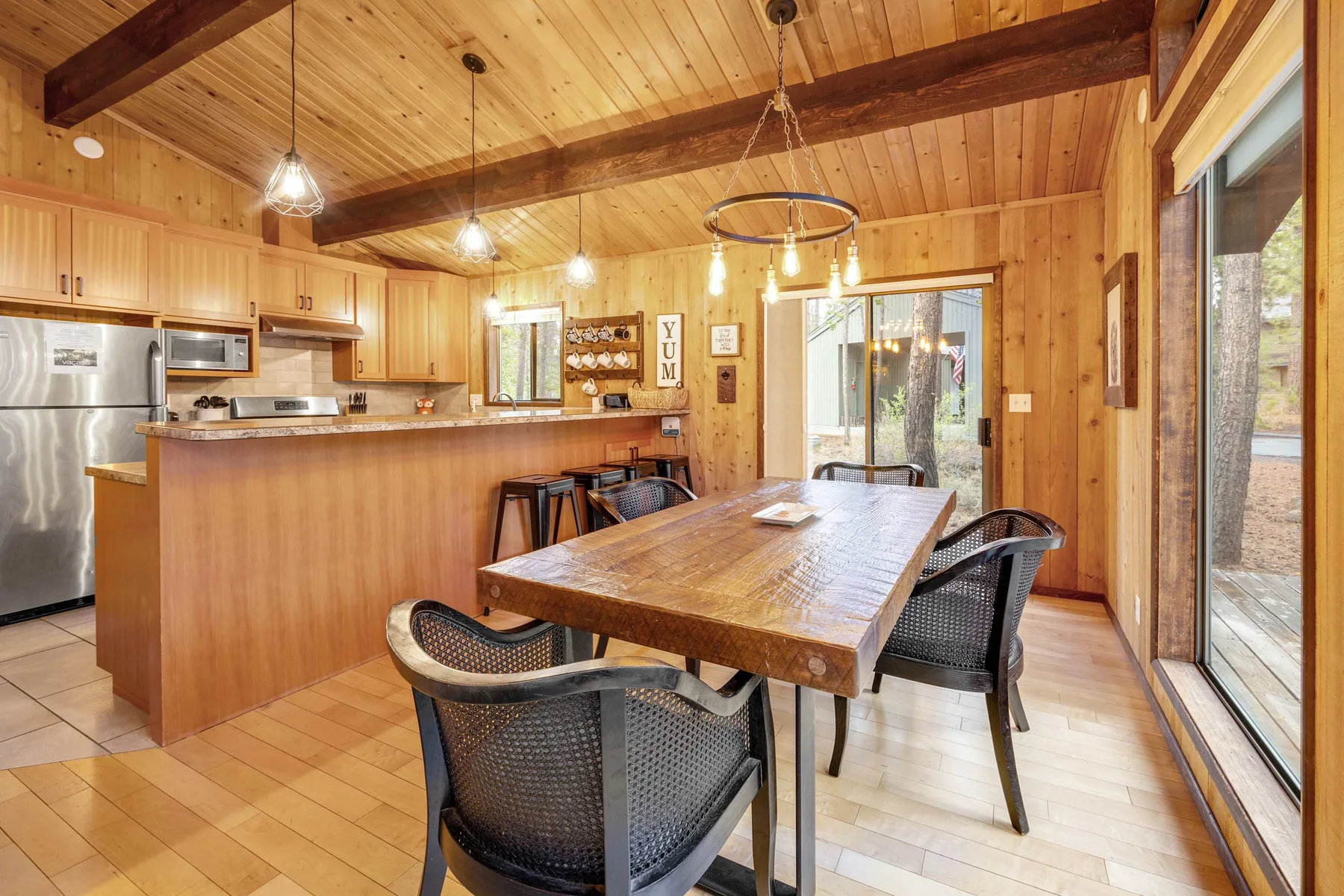 Cocina y comedor revestidos de madera, con una mesa grande junto a puertas corredizas de vidrio.