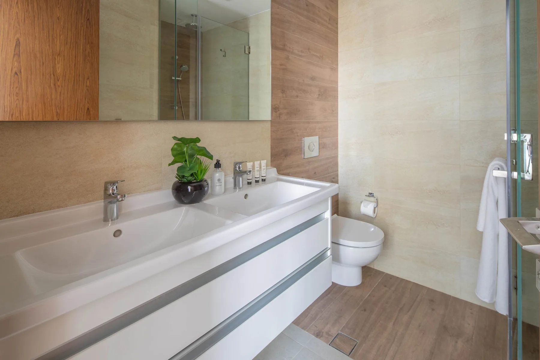 Un baño con un largo mueble de doble lavabo y una ducha de vidrio.