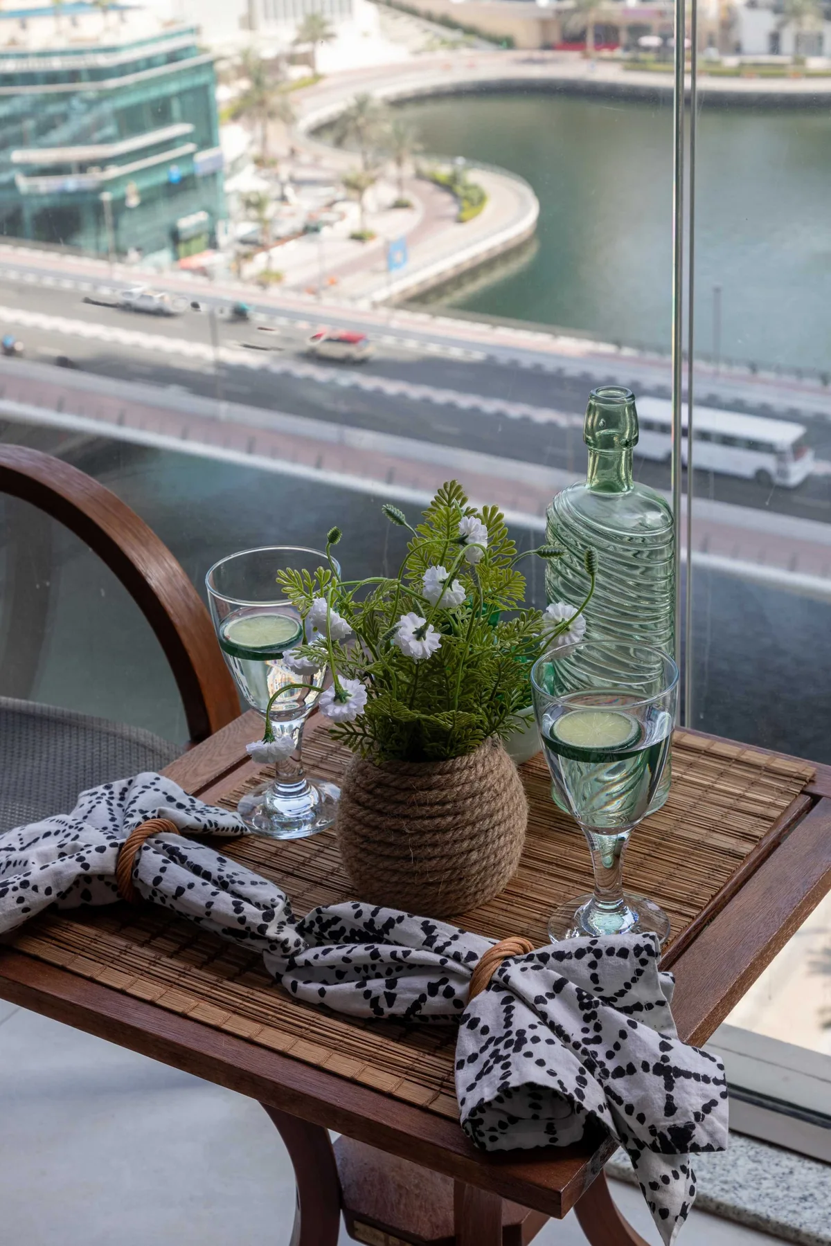 Una mesa pequeña junto a una ventana tiene plantas, copas y tela estampada doblada.