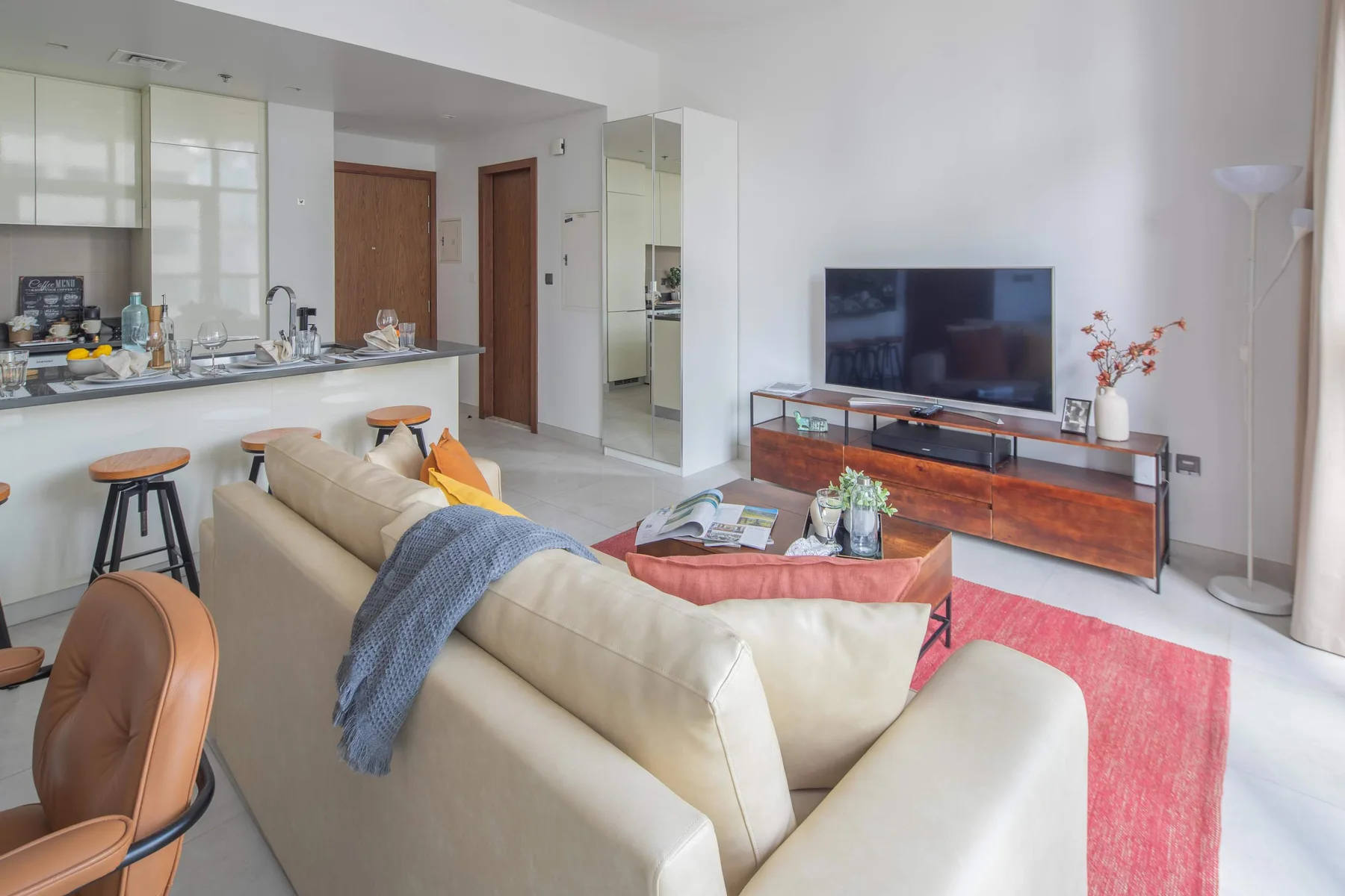 Una sala luminosa con televisor, asientos y una pequeña zona de cocina.