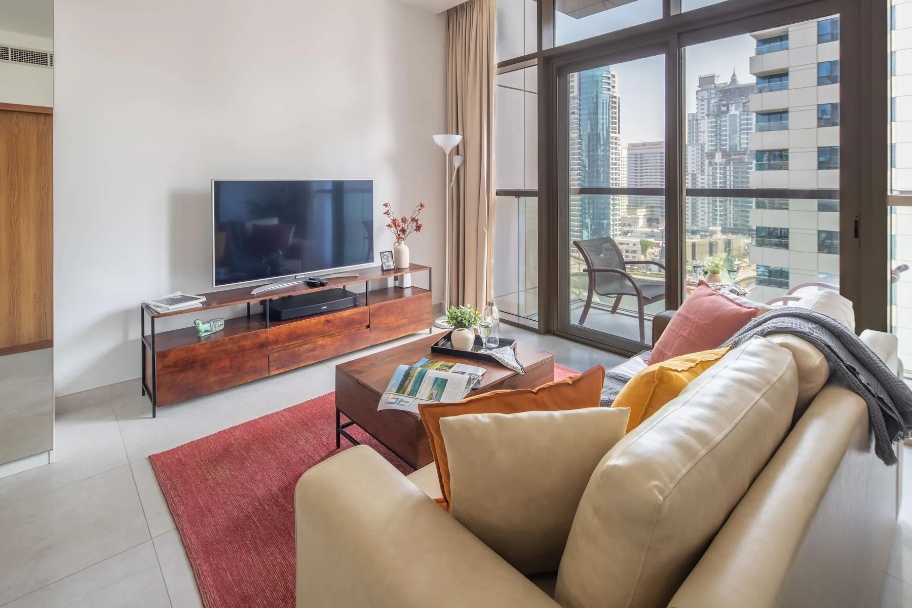 Una sala de estar con asientos, un televisor y grandes ventanas con edificios cercanos a la vista.