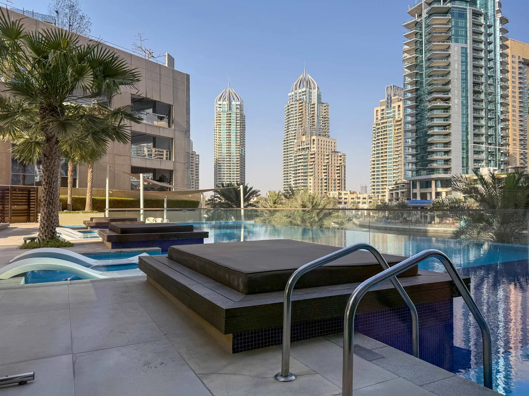 Terraza con piscina y una plataforma elevada para sentarse, con edificios altos al fondo.