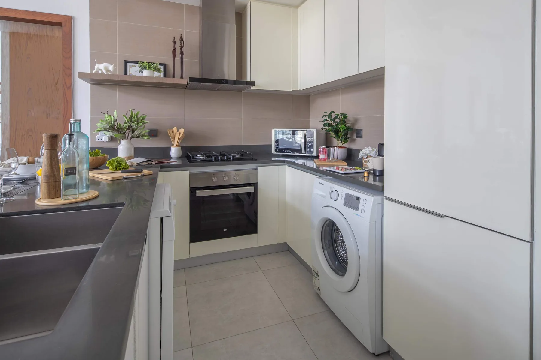 Una cocina compacta con armarios blancos, una placa de cocina y una lavadora.