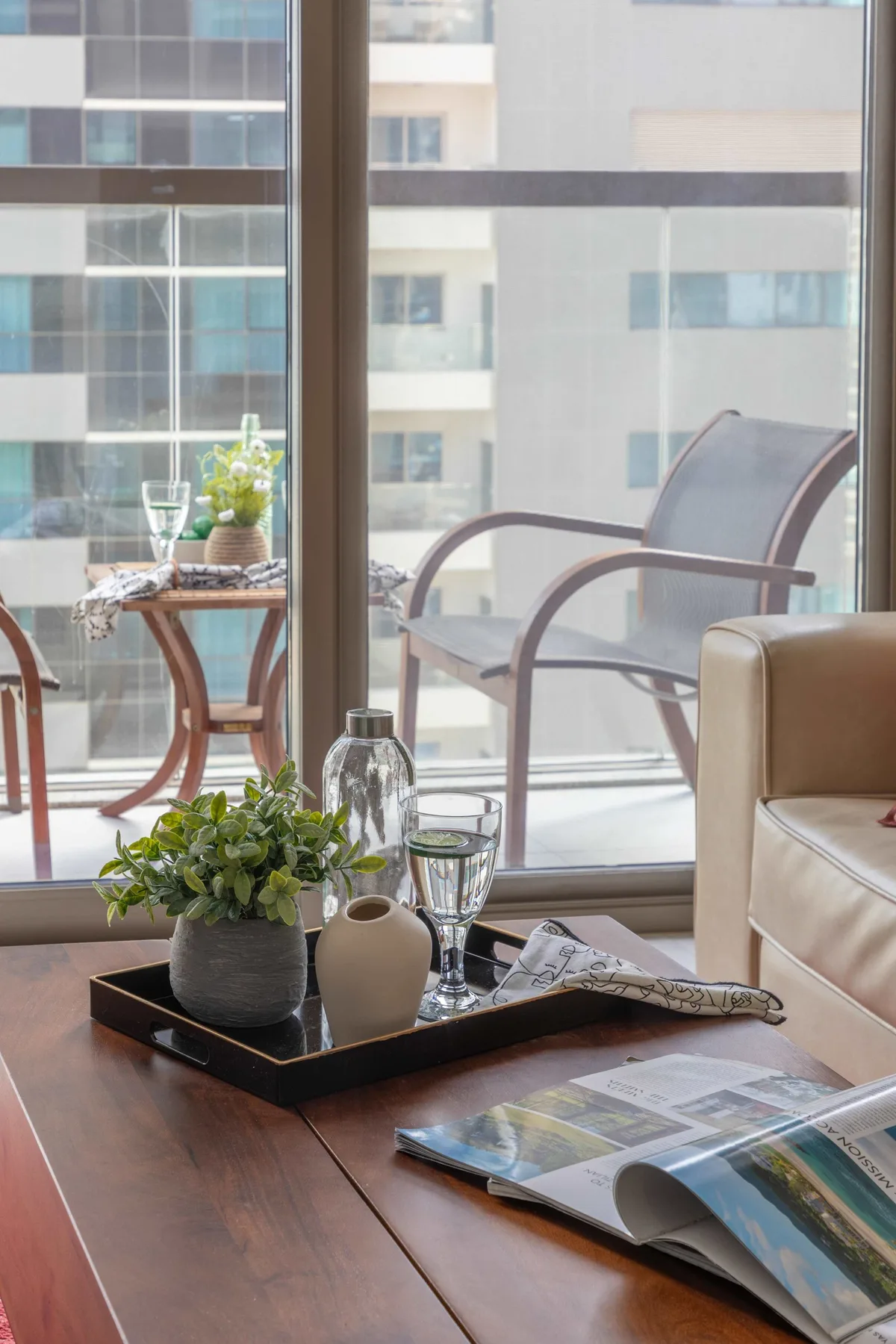 Una luminosa sala de estar con mesa de centro, asientos y grandes ventanales con vista a edificios cercanos.