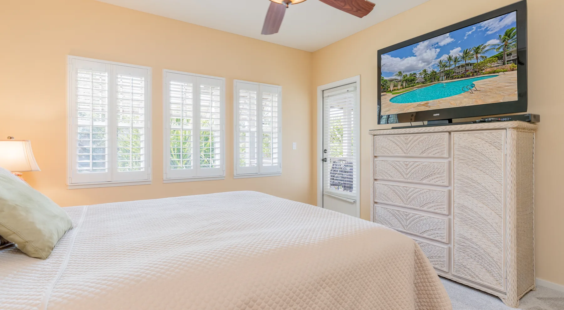 Un dormitorio con una cama, ventanas con persianas y un televisor sobre una cómoda.