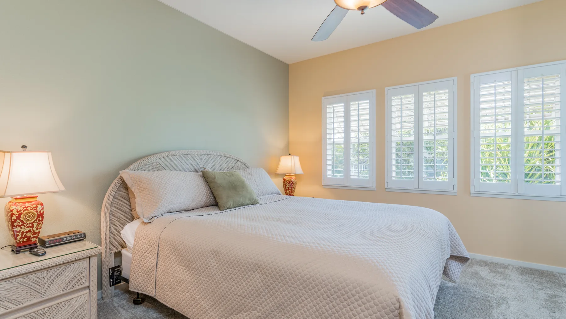 Un dormitorio con una cama bien hecha y ventanas con contraventanas.