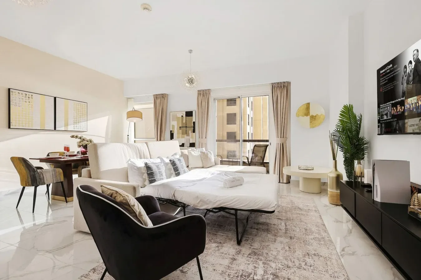 Una sala luminosa con un sofá blanco, un sillón negro y grandes ventanas.