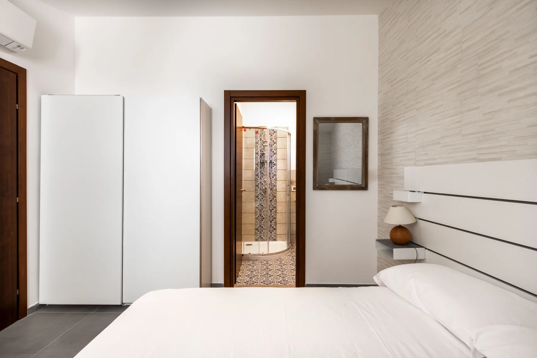 A bedroom with a bed and an open doorway to a tiled shower.