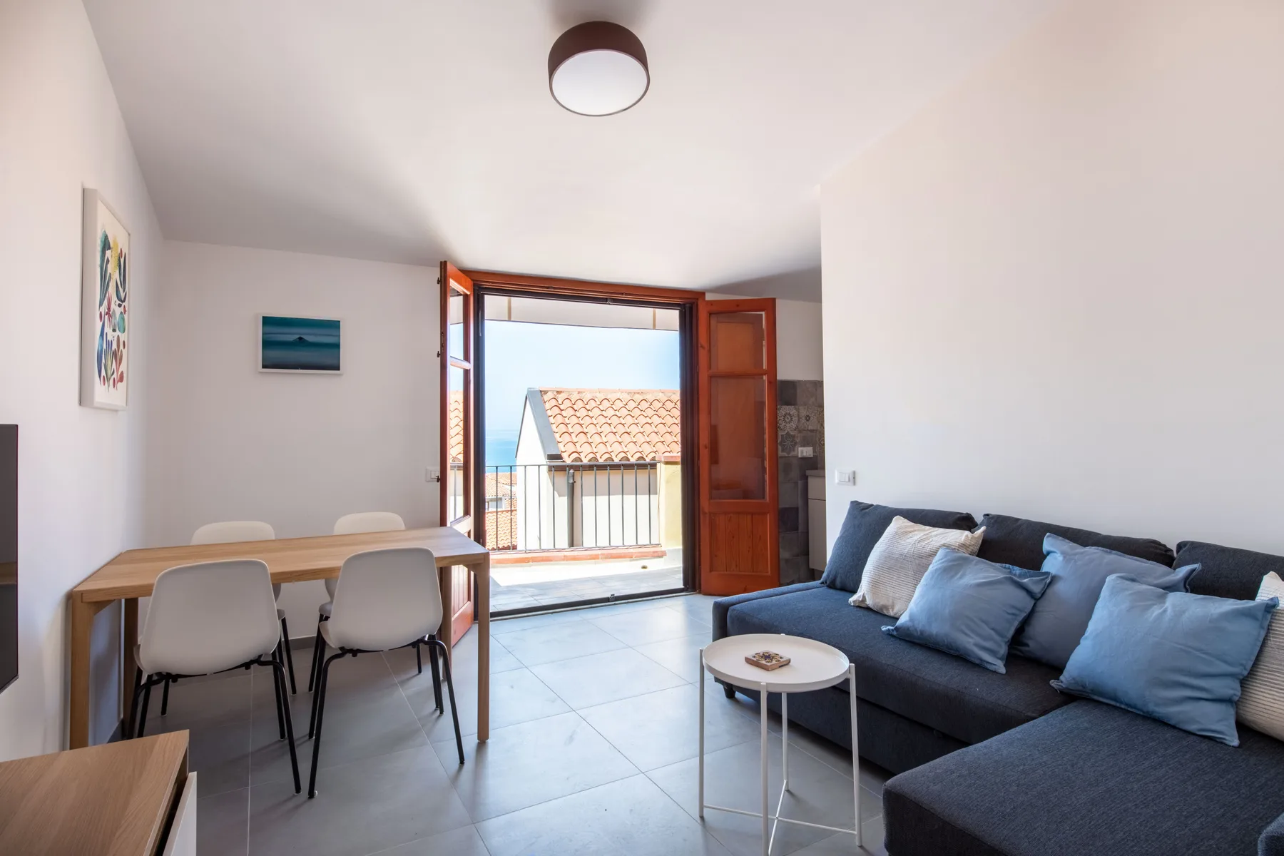 A bright living and dining area opens onto a balcony through open doors.