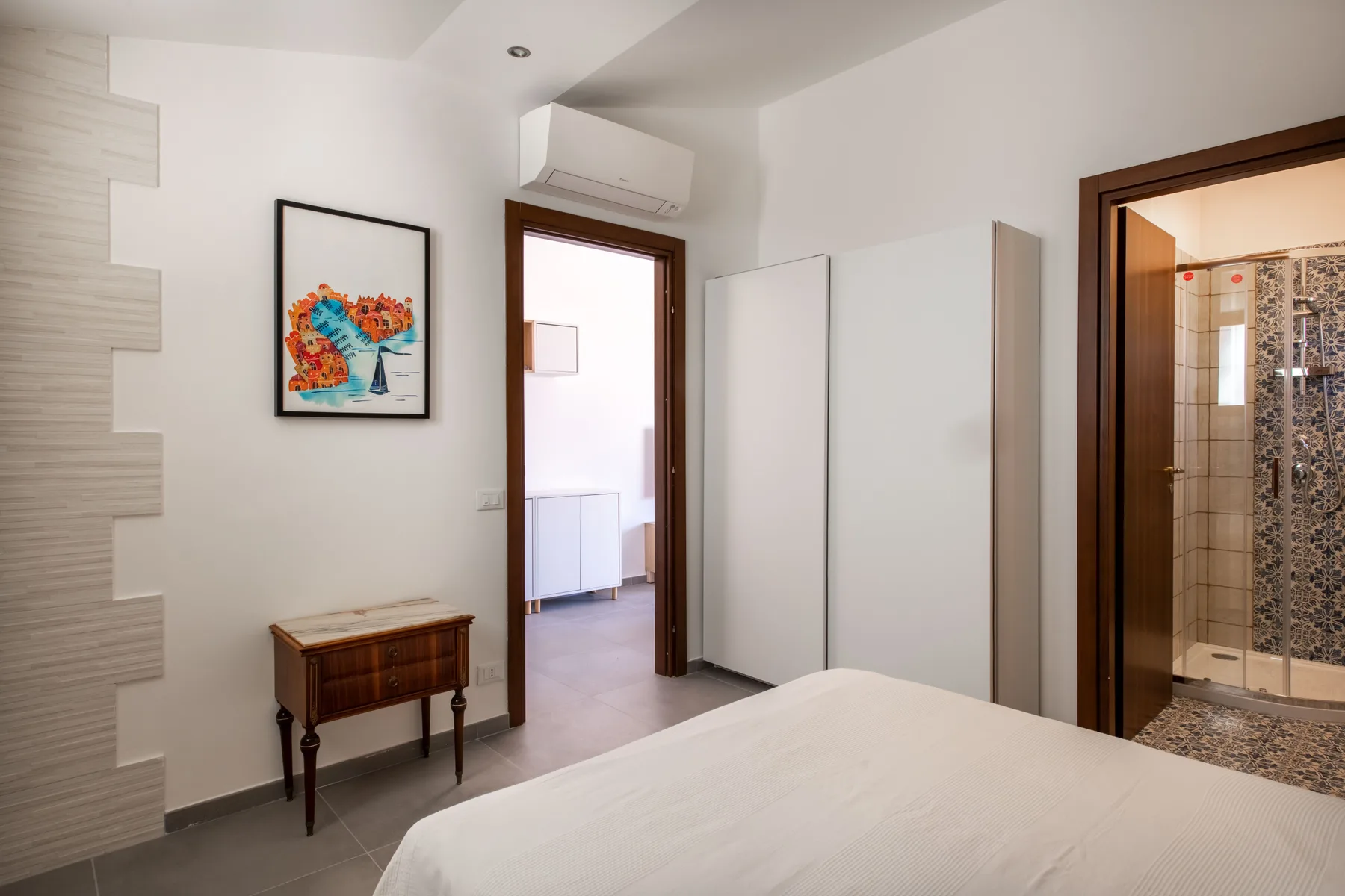 Un dormitorio con una cama, una mesa pequeña de madera y una puerta al baño.