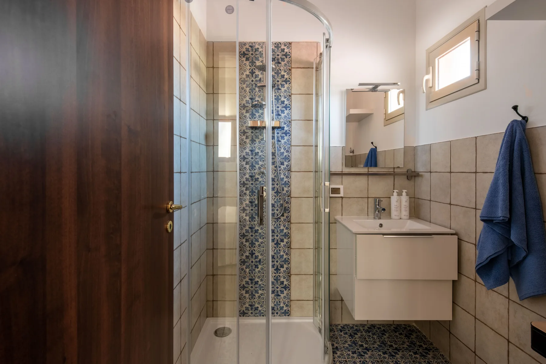 Un baño alicatado con una ducha de vidrio y un lavabo suspendido.