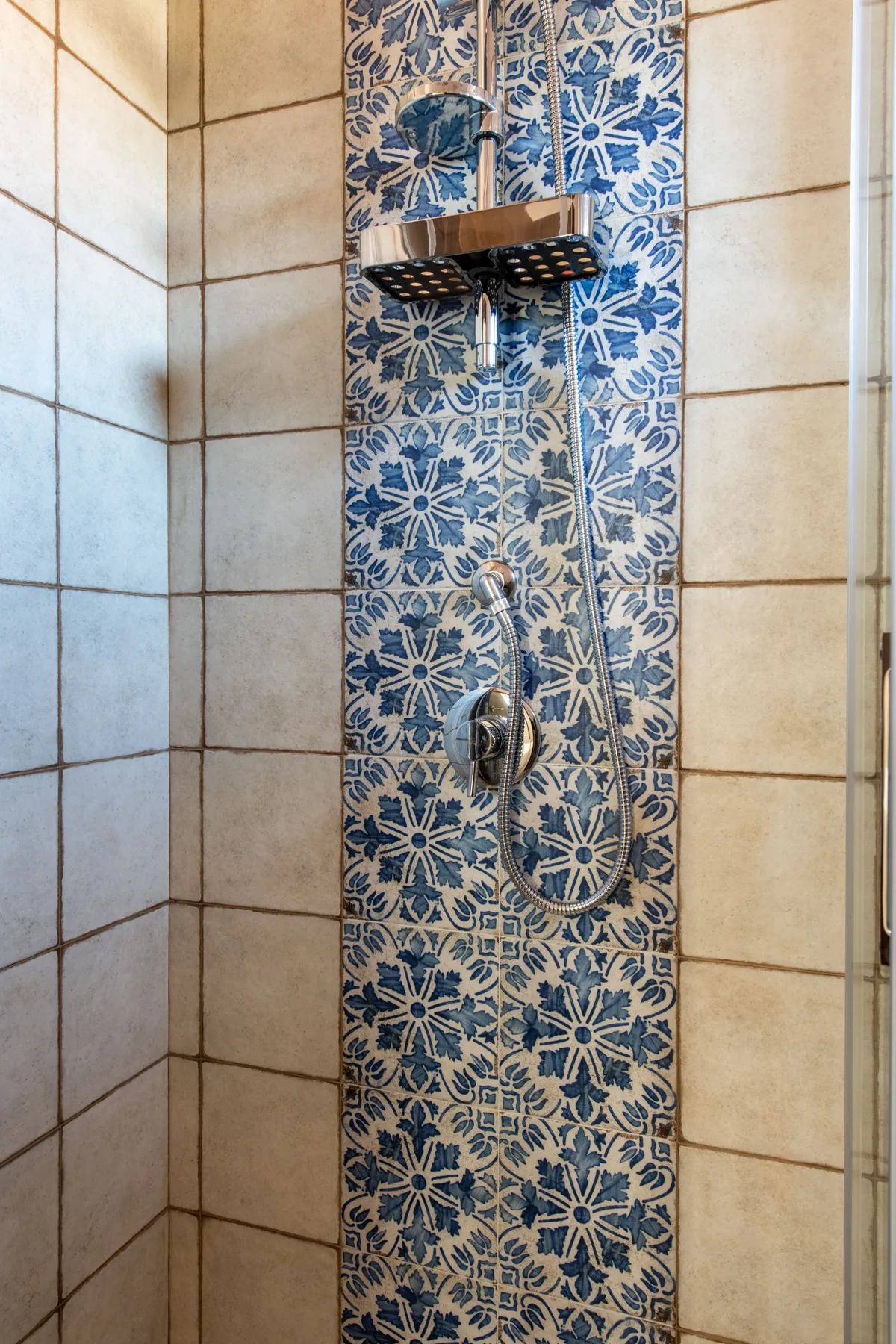 Una ducha alicatada con un panel azul estampado y sus accesorios.