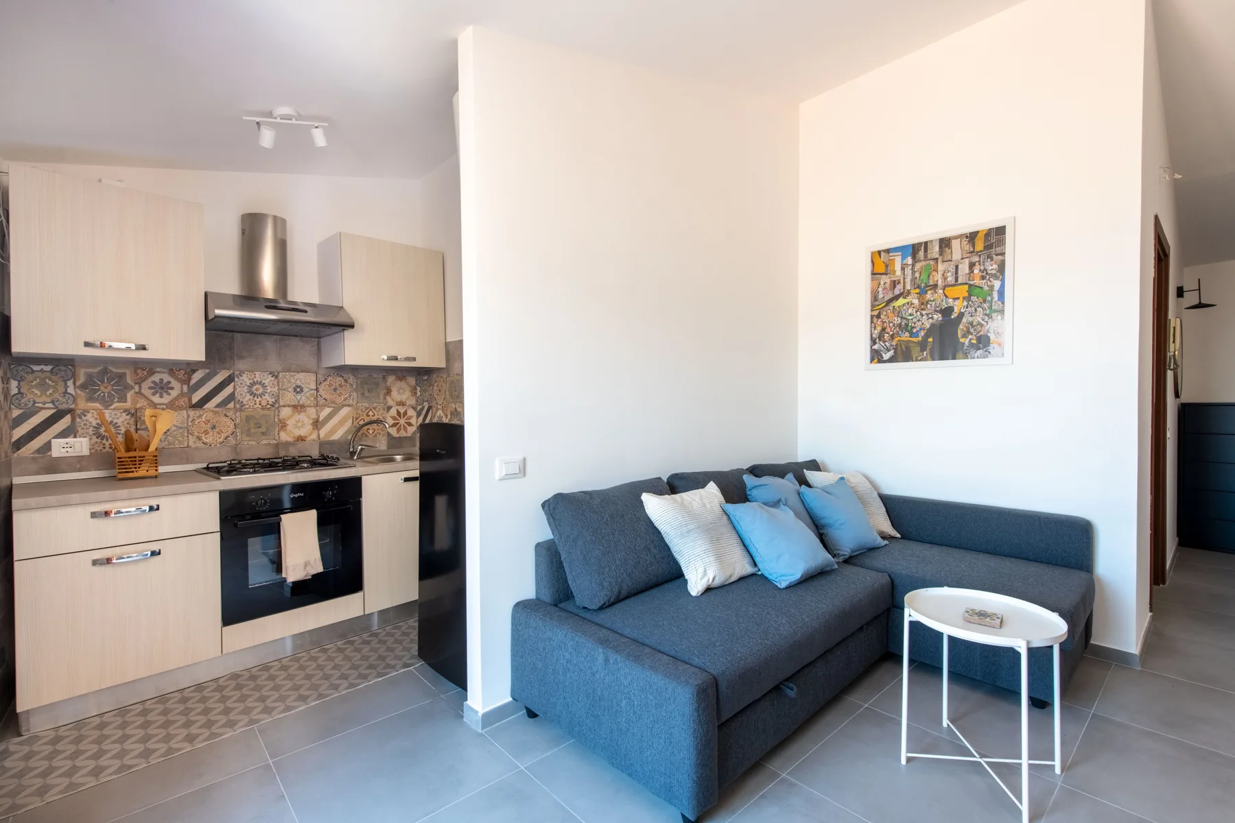 A living area with a blue sectional sofa beside a compact kitchen.