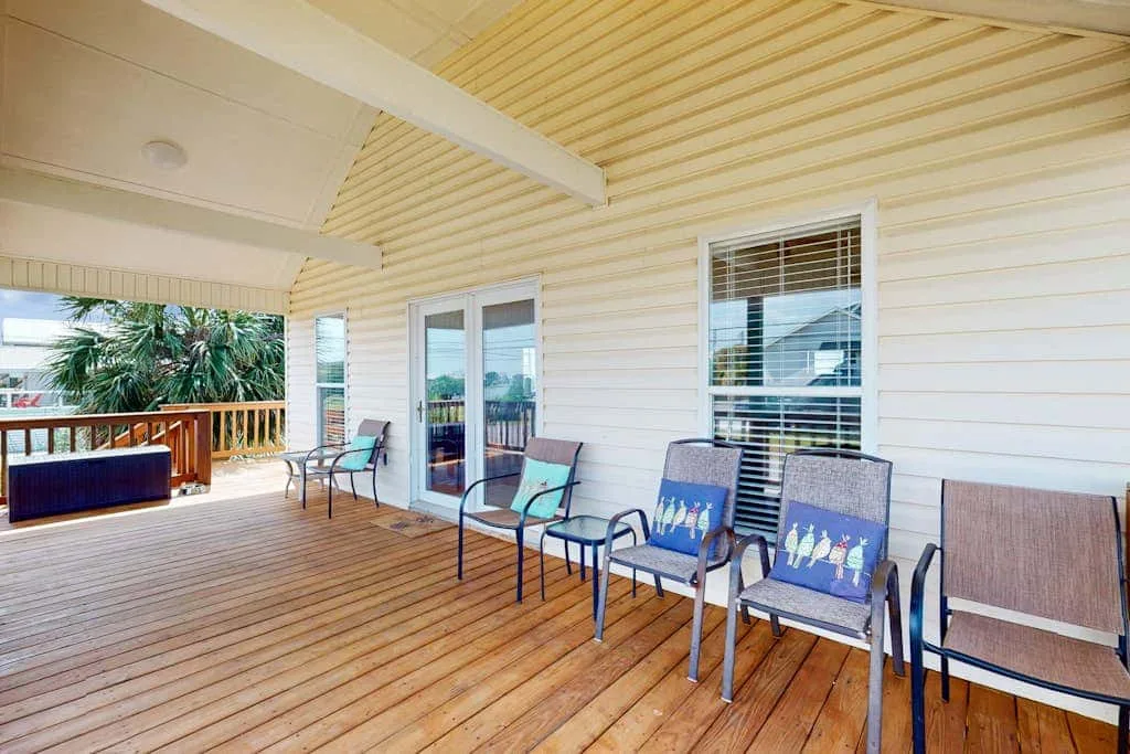 A covered wooden deck with several chairs and glass doors along the wall.
