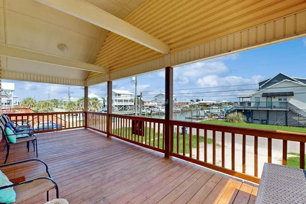Covered outdoor deck with wooden railings and seating overlooking nearby homes.
