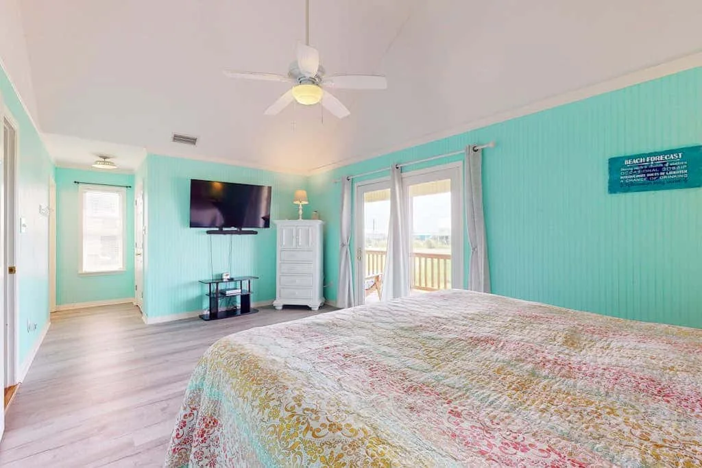 A bedroom with a patterned bedspread, television, and glass doors opening to a balcony.