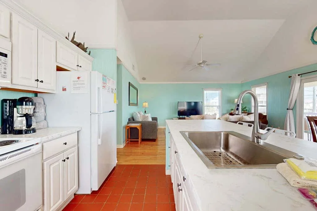 A bright kitchen opens onto a living area, with a large island and sink.