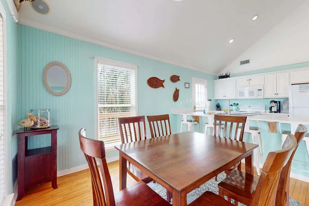 A dining area with a wooden table and chairs beside a bright kitchen.