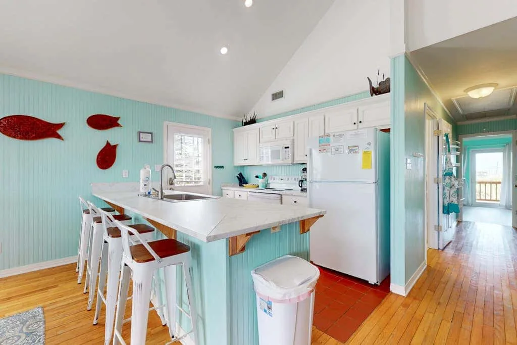 A bright kitchen with a long counter and white cabinets opens onto a hallway.