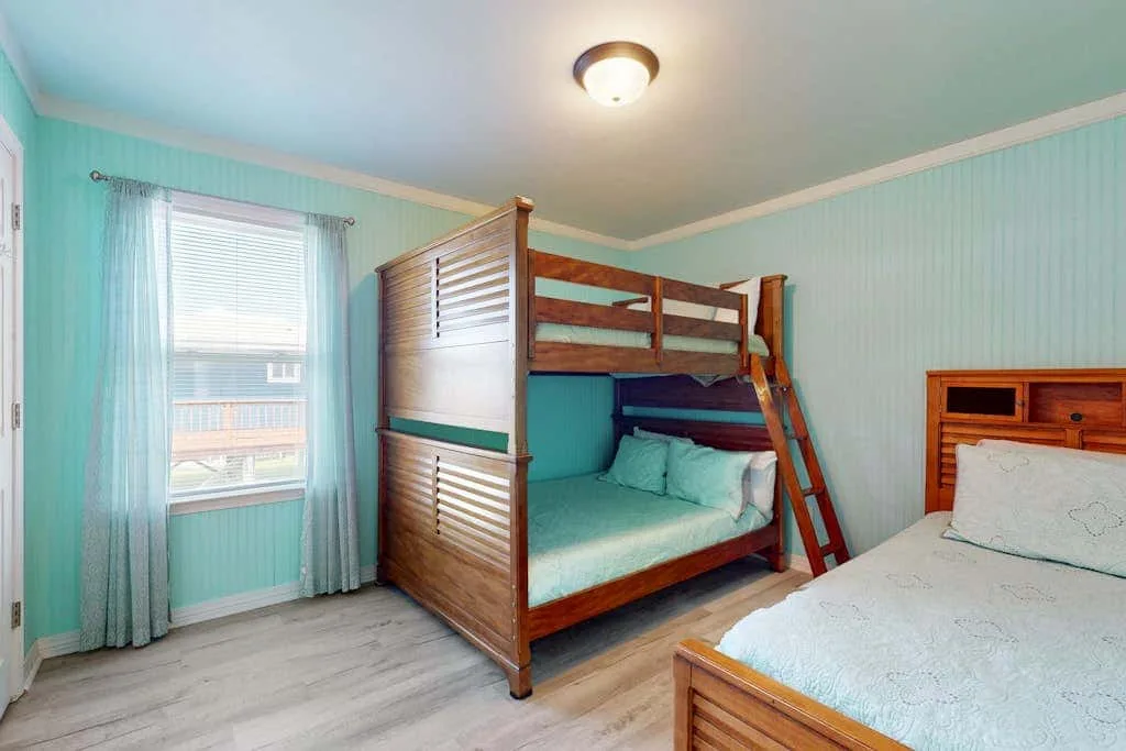 A bedroom with a wooden bunk bed and a window with pale curtains.