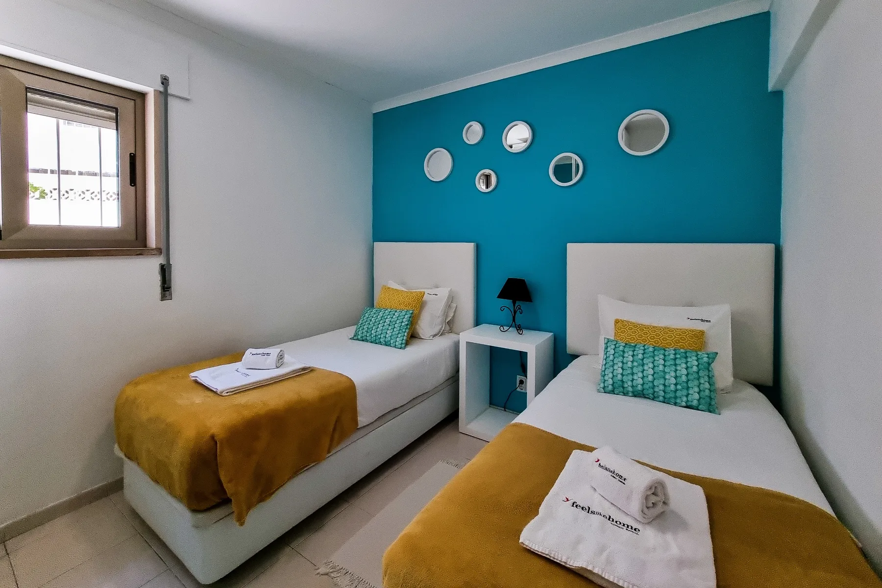 A bedroom with two single beds, mustard-colored blankets, and a teal accent wall.