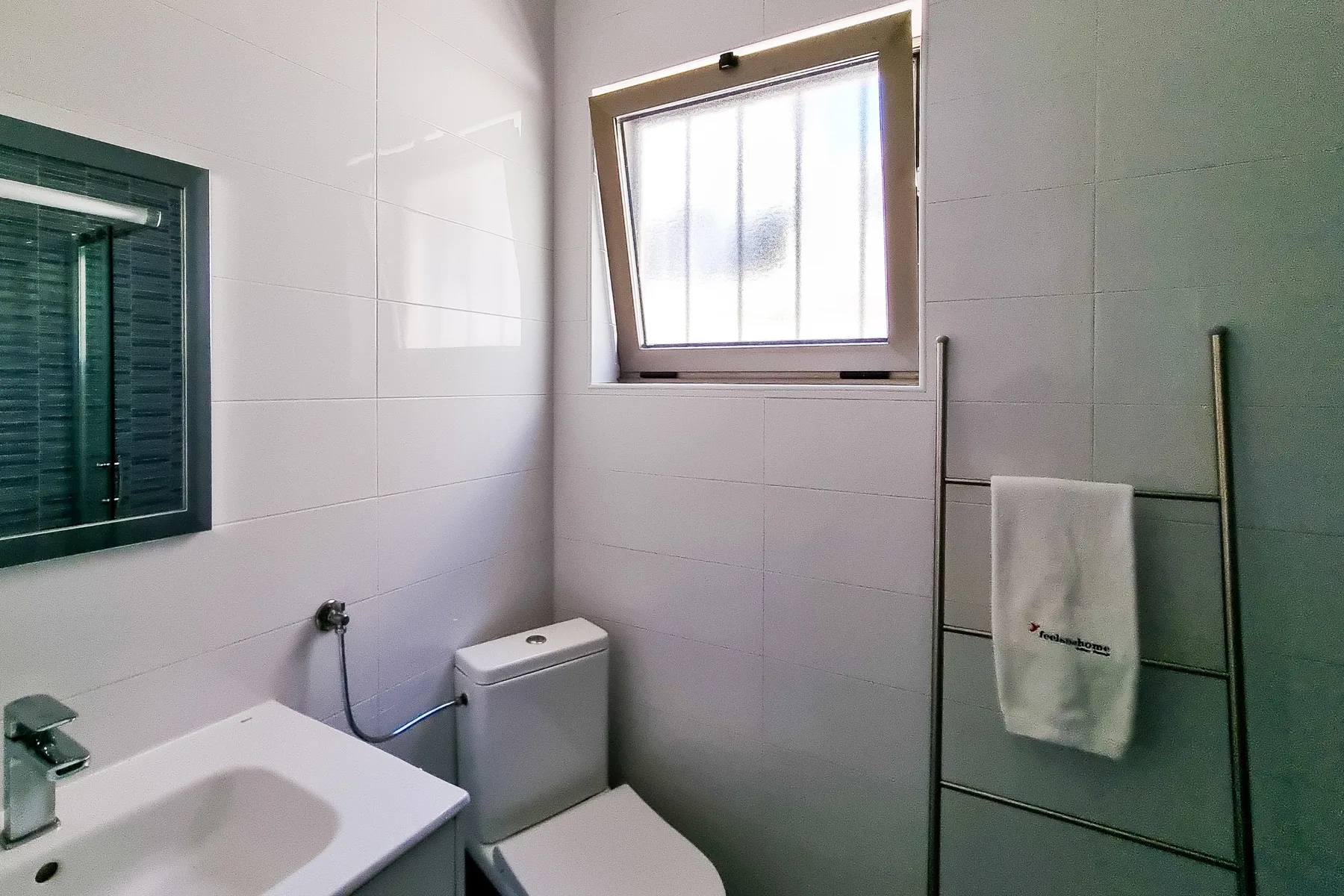 Un baño alicatado con lavabo, inodoro y una ventana pequeña.