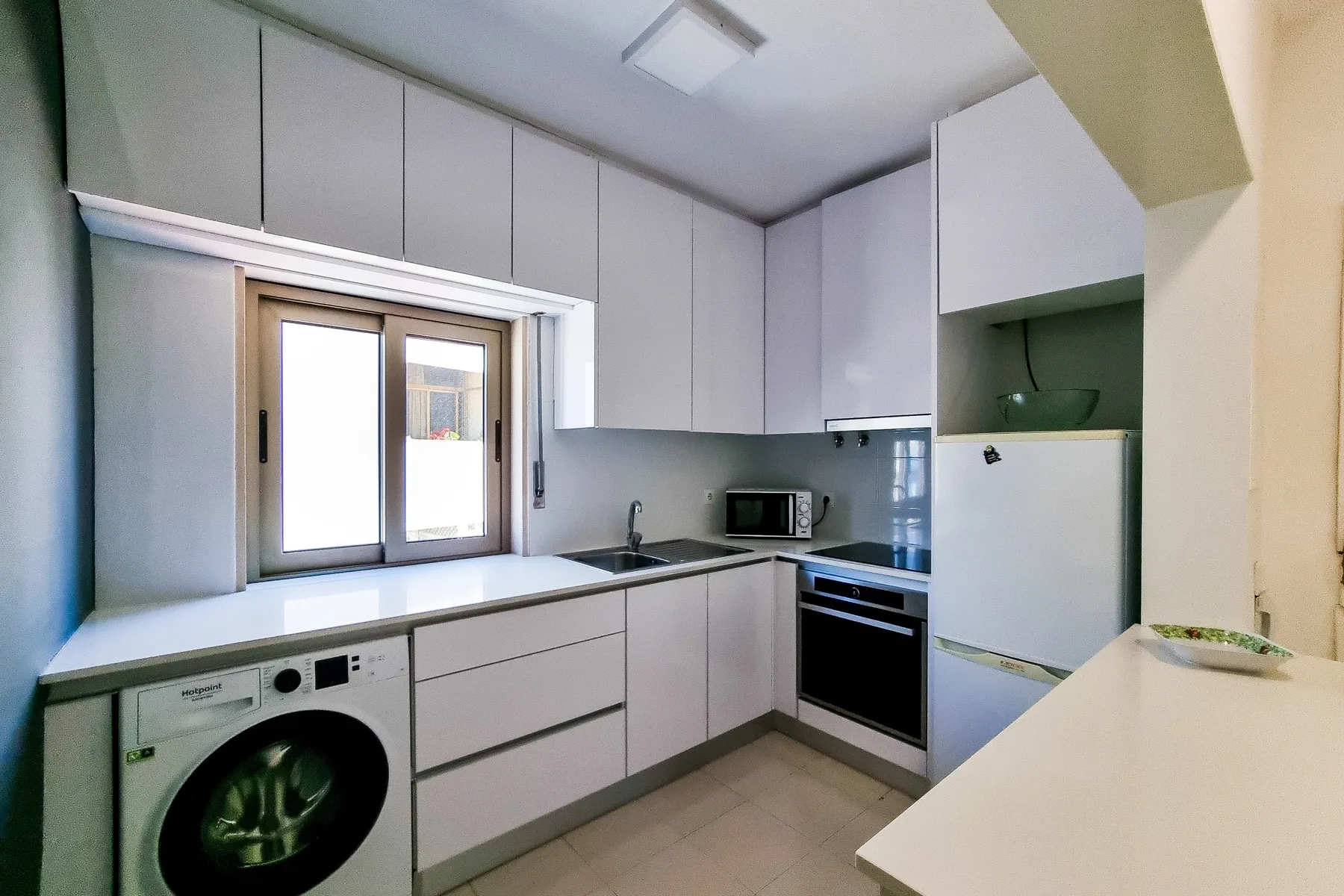 Una cocina compacta con armarios blancos, electrodomésticos y una ventana.
