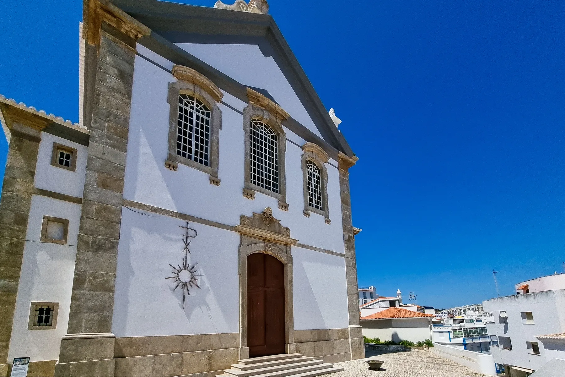 A white building with stone trim and a wooden entrance stands beneath a clear blue sky.