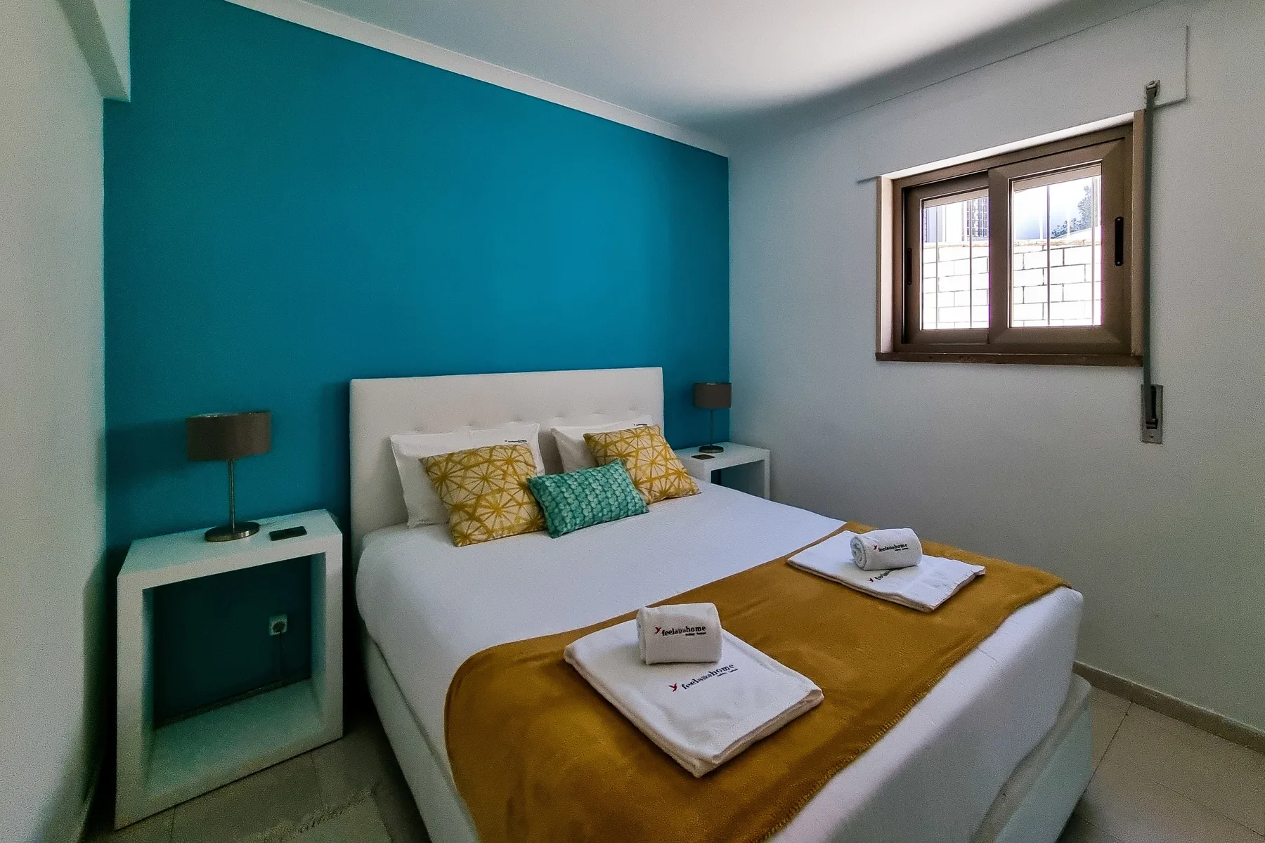 A bedroom with a bed against a teal accent wall and a window.