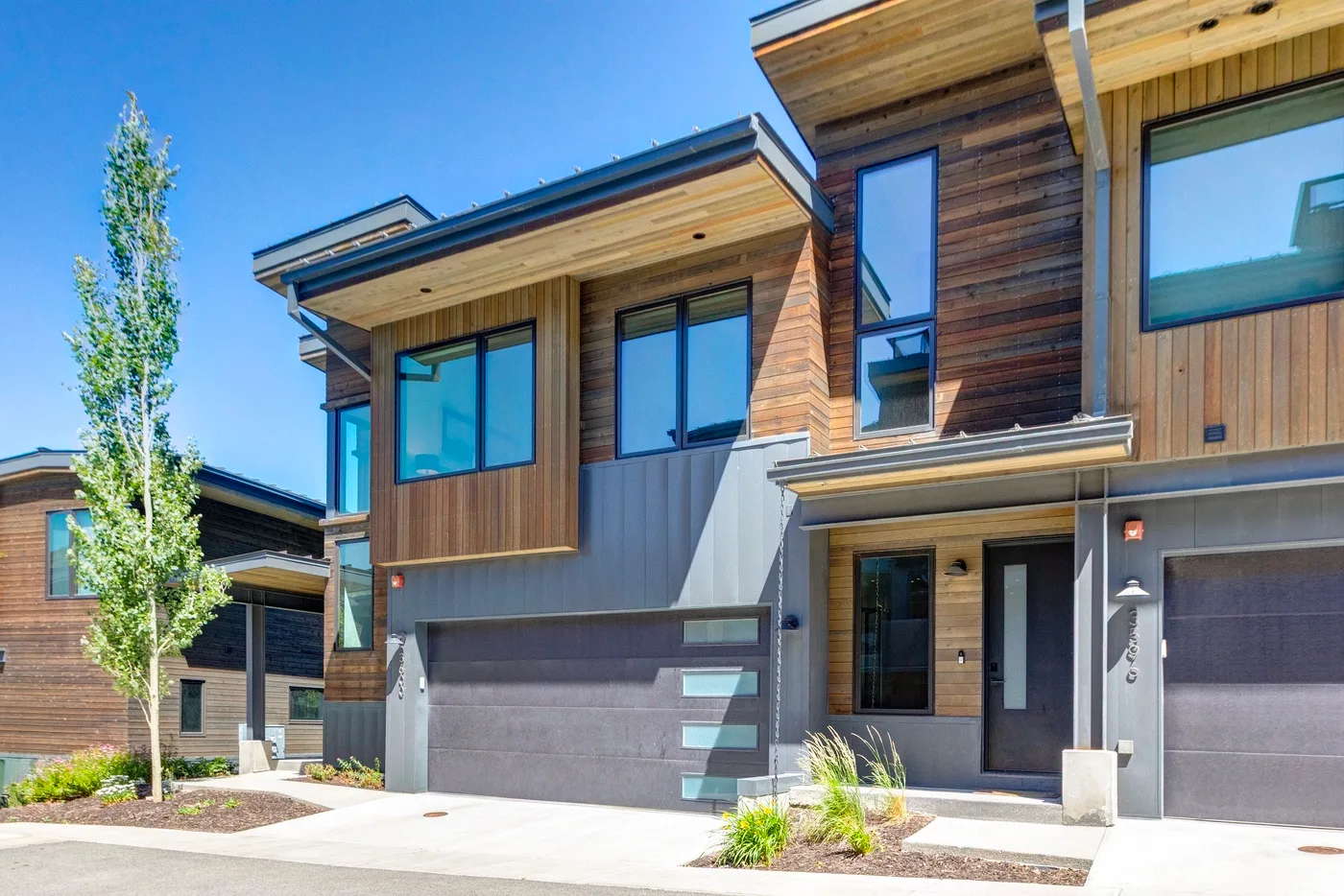 Exterior de una casa moderna de varios niveles, con revestimiento de madera, ventanas grandes y entrada para autos.
