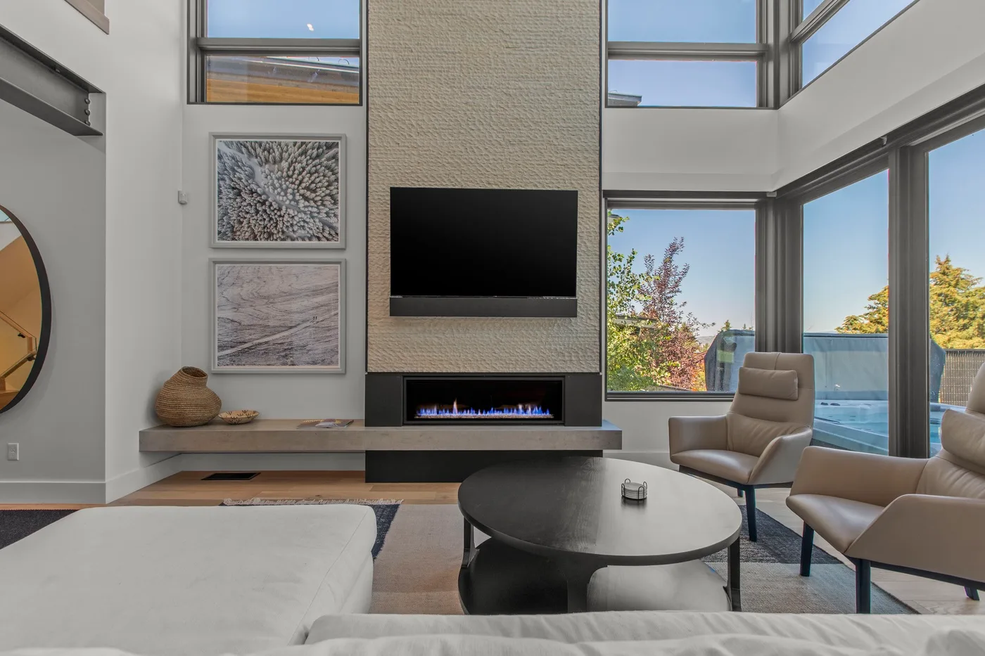 Una sala de estar luminosa con un televisor en la pared y asientos junto a grandes ventanas.