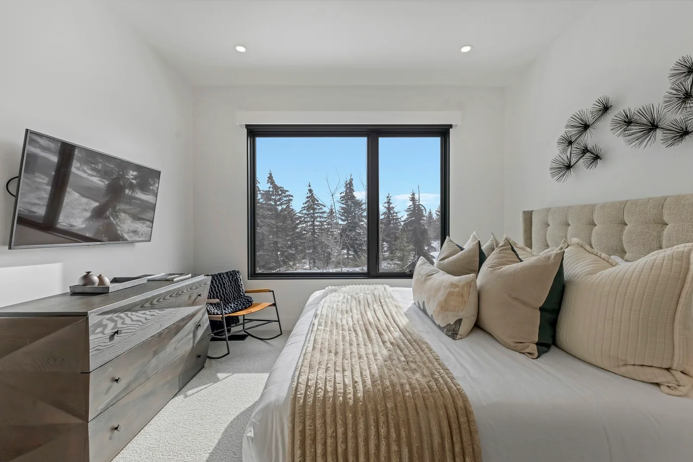 Un dormitorio luminoso con una cama grande, un asiento y una ventana con vistas a los árboles.