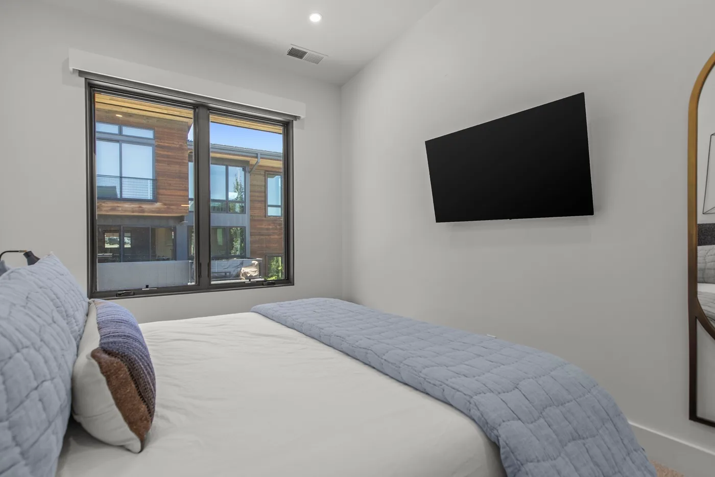 Un dormitorio con una cama, una ventana grande y un televisor en la pared.
